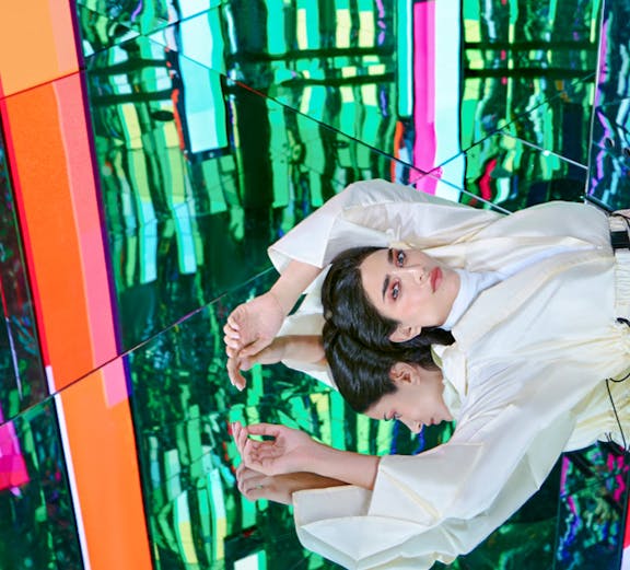 Person in white outfit reflected in colorful mirrored room at AYA Universe.