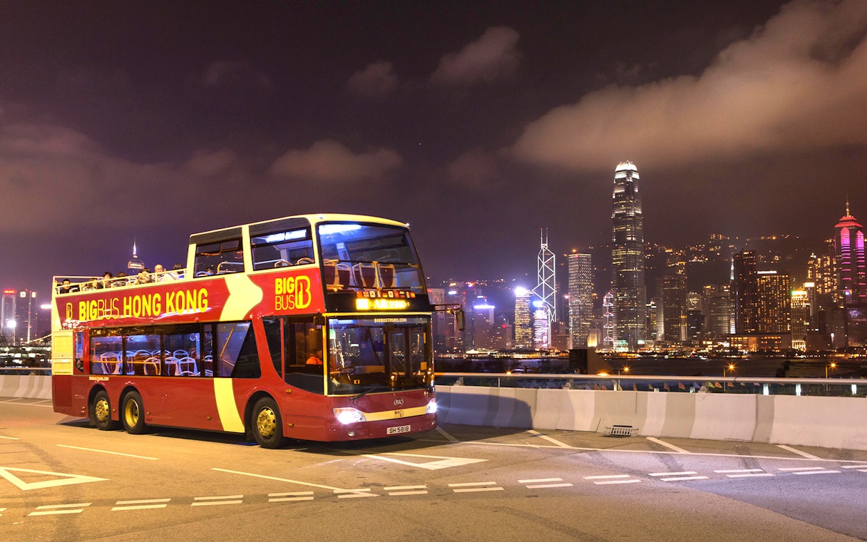 Hop-on-hop-off bus in Hong Kong with city skyline at night.