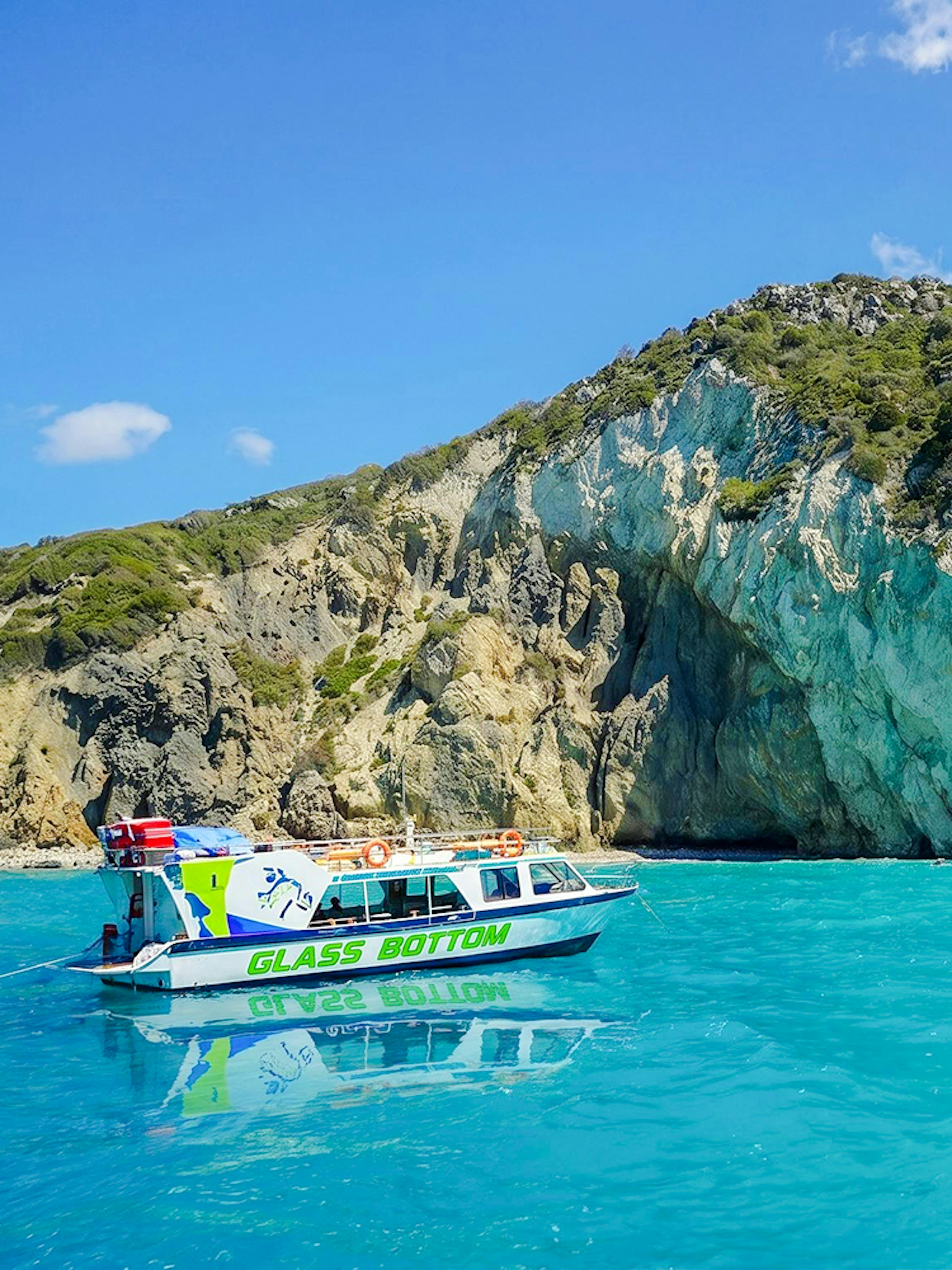 Glass bottom boat on turquoise waters near rocky cliffs in Zakynthos.