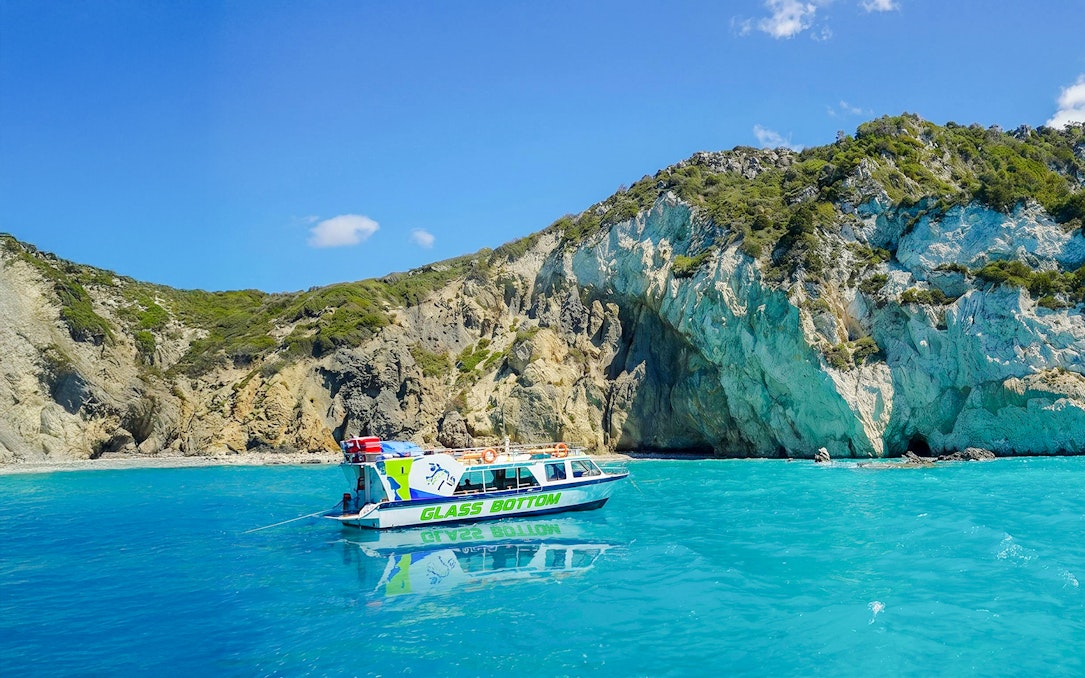Glass bottom boat on turquoise waters near rocky cliffs in Zakynthos.