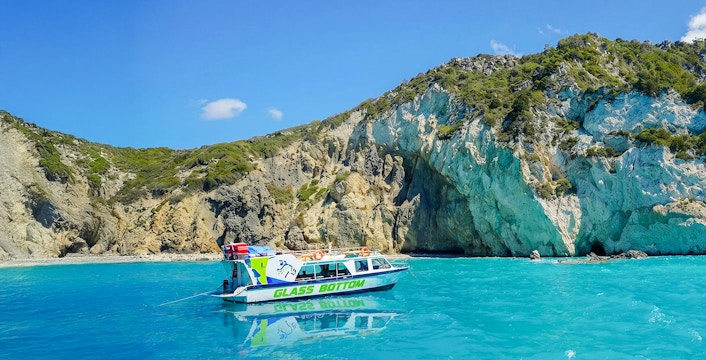 Glass bottom boat on turquoise waters near rocky cliffs in Zakynthos.