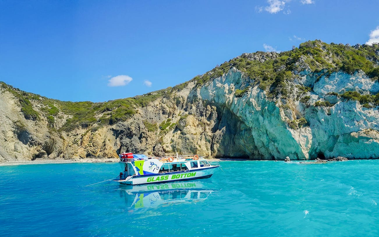 Glass bottom boat on turquoise waters near rocky cliffs in Zakynthos.