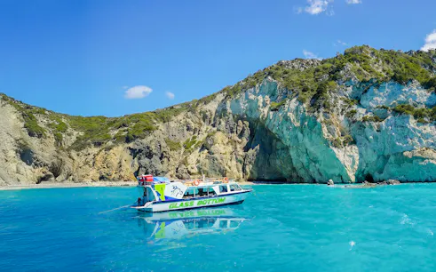 Glass bottom boat on turquoise waters near rocky cliffs in Zakynthos.