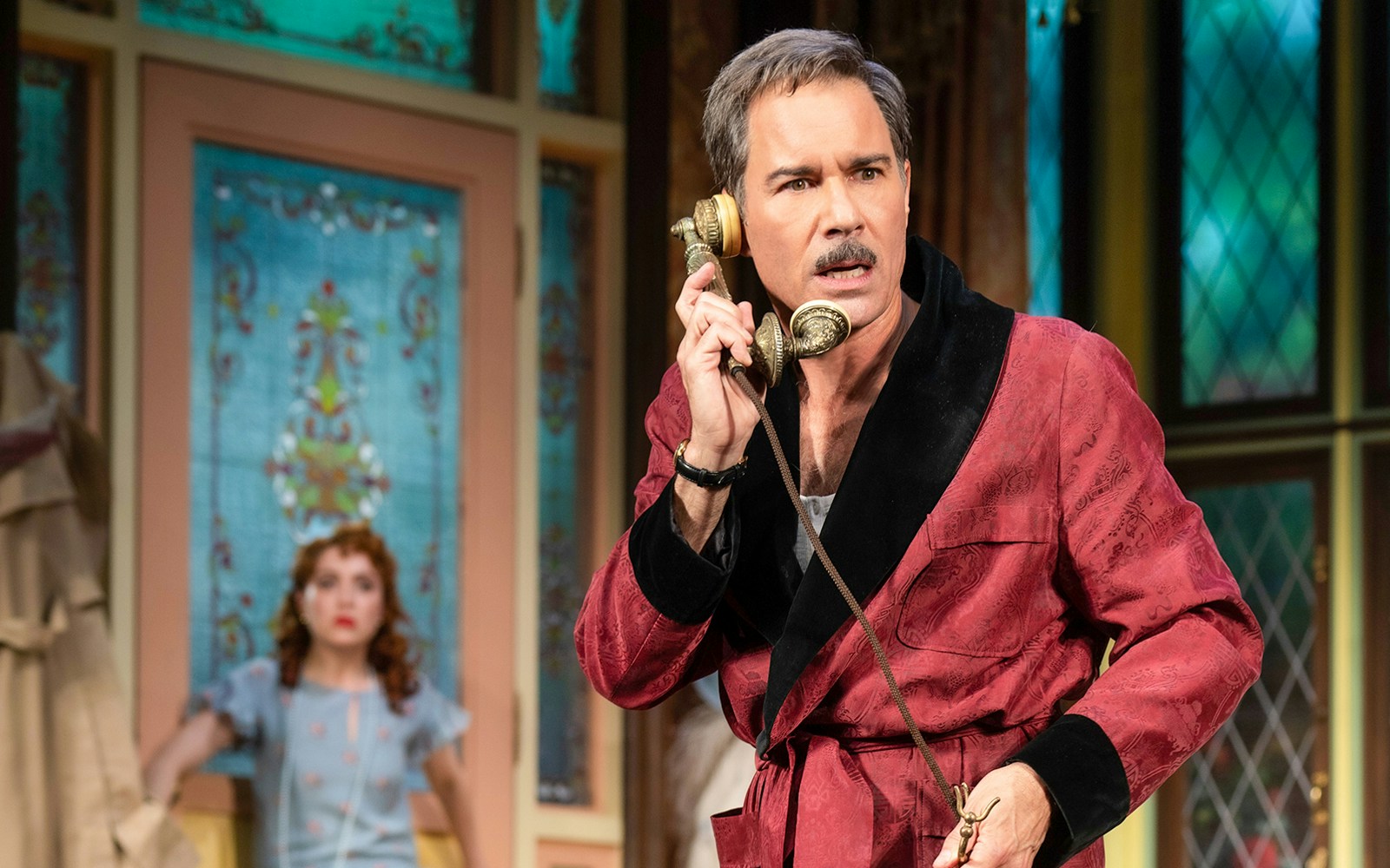 Man in red robe holding vintage phone in The Cottage play scene.