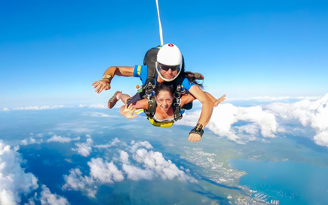 Tandem skydivers over Airlie Beach coastline with ocean and landscape below.