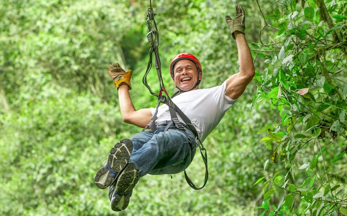 Person ziplining through lush forest at Waitomo Caves Zipline Park.