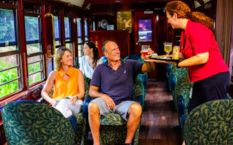 Passengers enjoying drinks on a scenic train tour with onboard service.