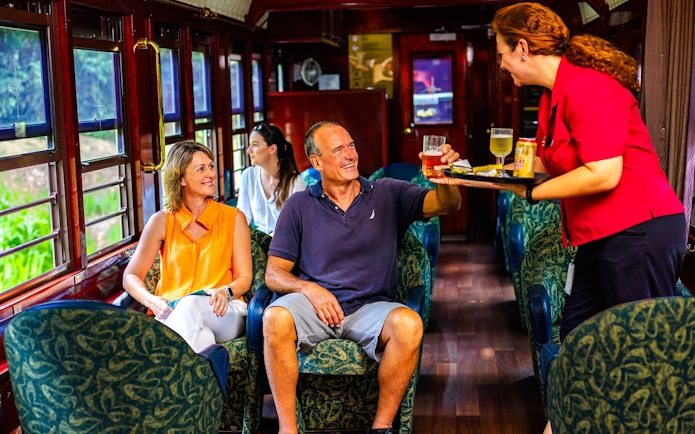 Passengers enjoying drinks on a scenic train tour with onboard service.