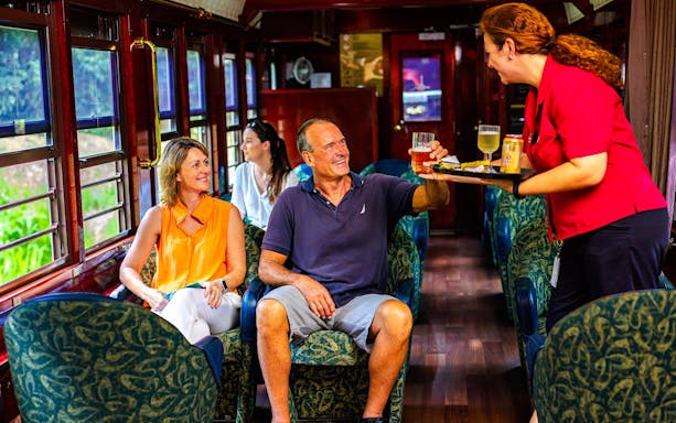 Passengers enjoying drinks on a scenic train tour with onboard service.