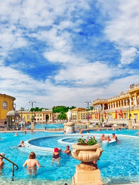 Visitors enjoying thermal pools at Szechenyi Bath, Budapest, with historic architecture in the background.