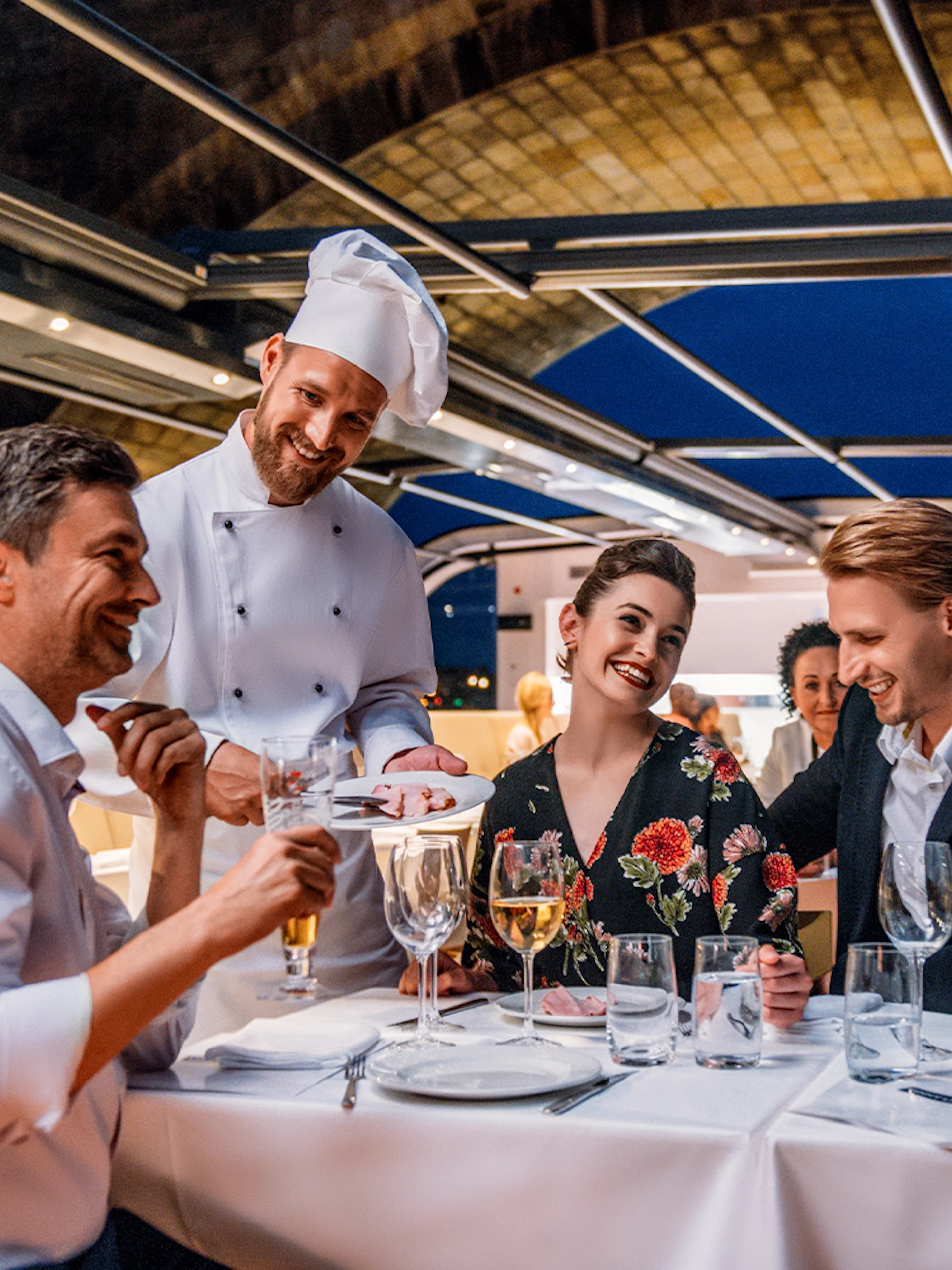 Dinner guests enjoying a meal on a Prague sightseeing cruise with a chef serving dishes.