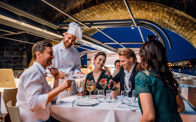 Dinner guests enjoying a meal on a Prague sightseeing cruise with a chef serving dishes.