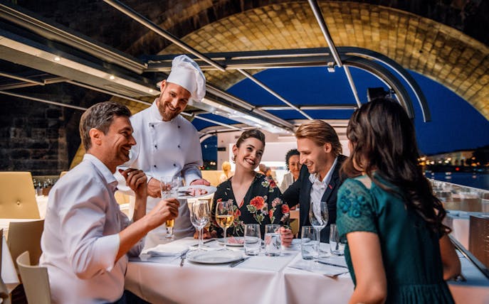 Dinner guests enjoying a meal on a Prague sightseeing cruise with a chef serving dishes.