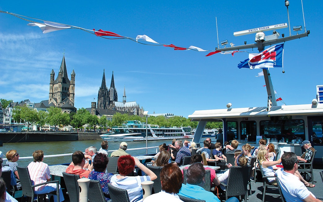 Tourists on a boat enjoying a panoramic view of Cologne Cathedral and Great St. Martin Church.