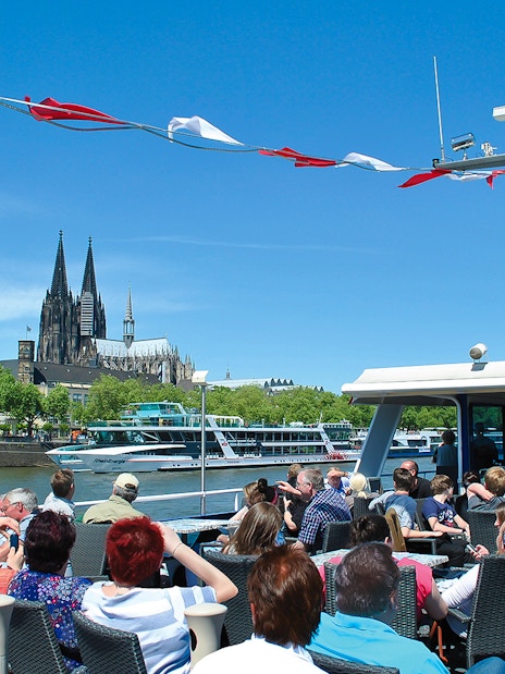 Tourists on a boat enjoying a panoramic view of Cologne Cathedral and Great St. Martin Church.