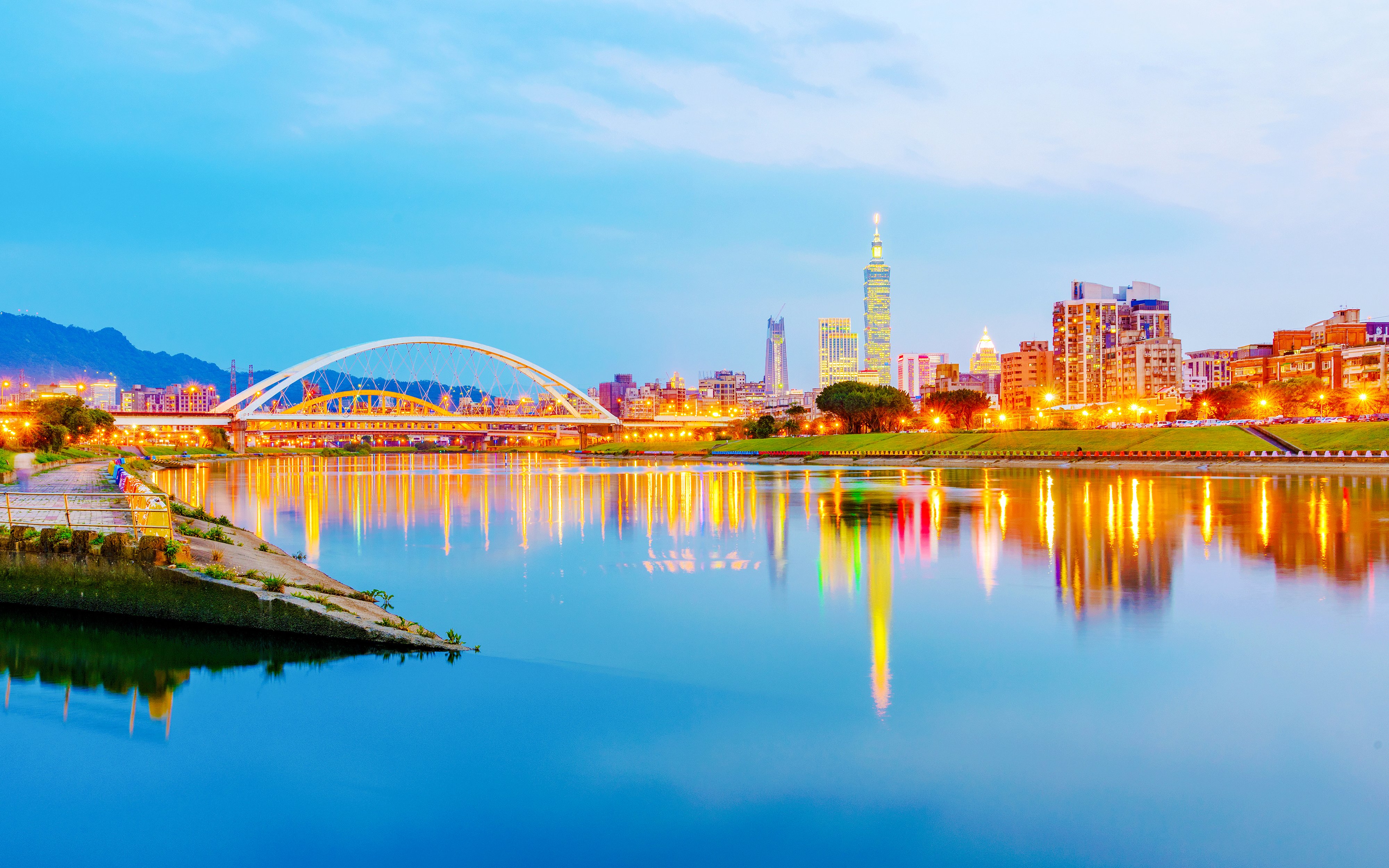 Keelung River with Taipei skyline and illuminated bridge at dusk.