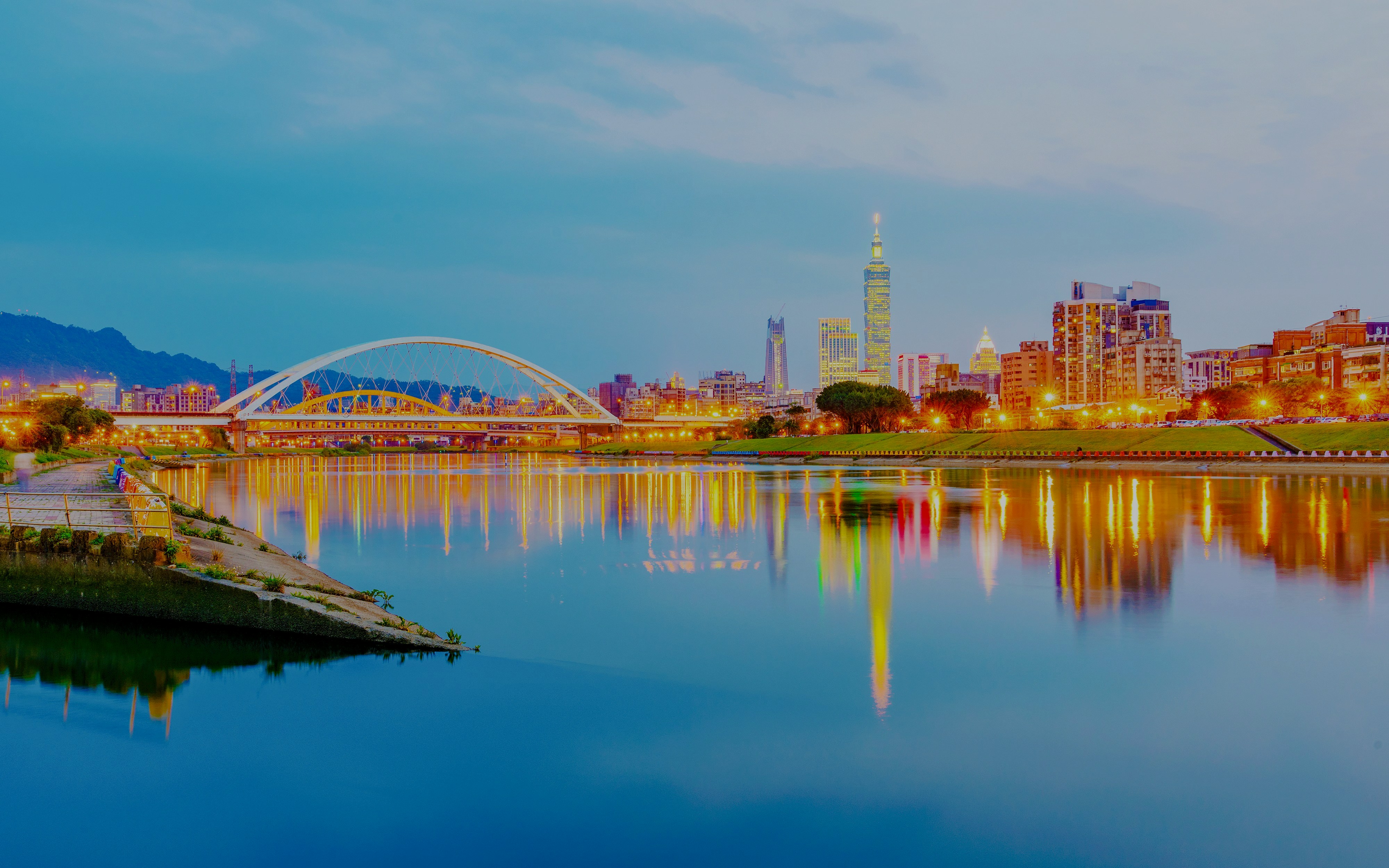 Keelung River with Taipei skyline and illuminated bridge at dusk.