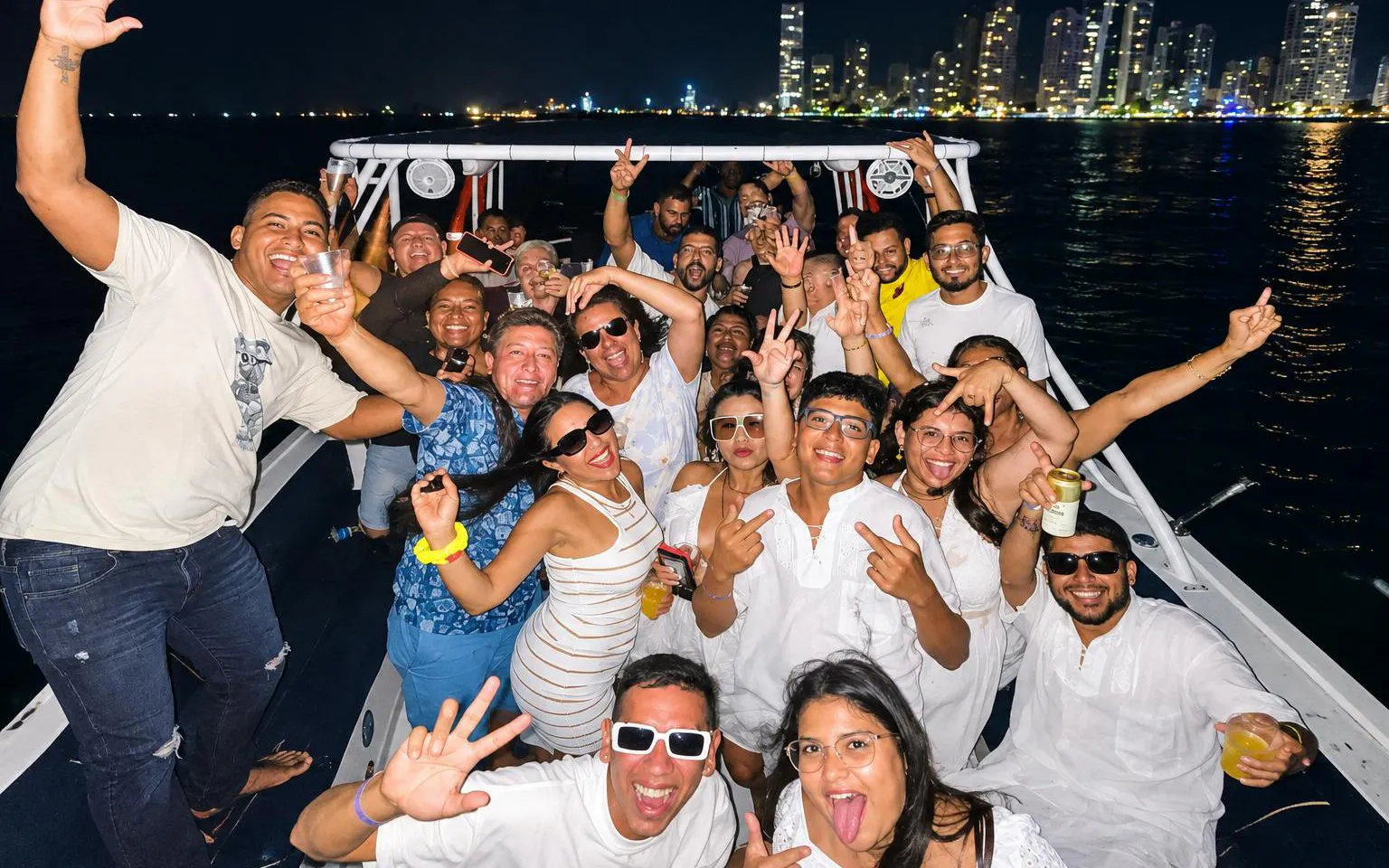 Group enjoying a lively sunset party cruise in Cartagena with city skyline in the background.