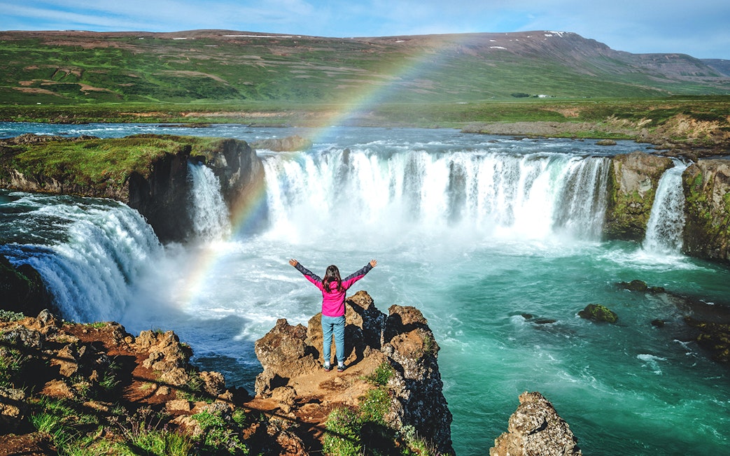 Tourist at Gullfoss waterfall in Iceland with a rainbow overhead.