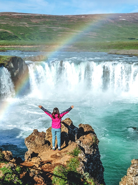 Tourist at Gullfoss waterfall in Iceland with a rainbow overhead.