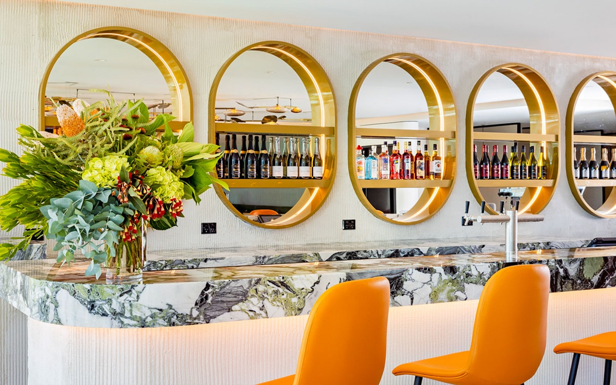 Plaza Premium Lounge bar with orange chairs, marble counter, and circular shelves displaying bottles.