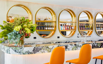 Plaza Premium Lounge bar with orange chairs, marble counter, and circular shelves displaying bottles.