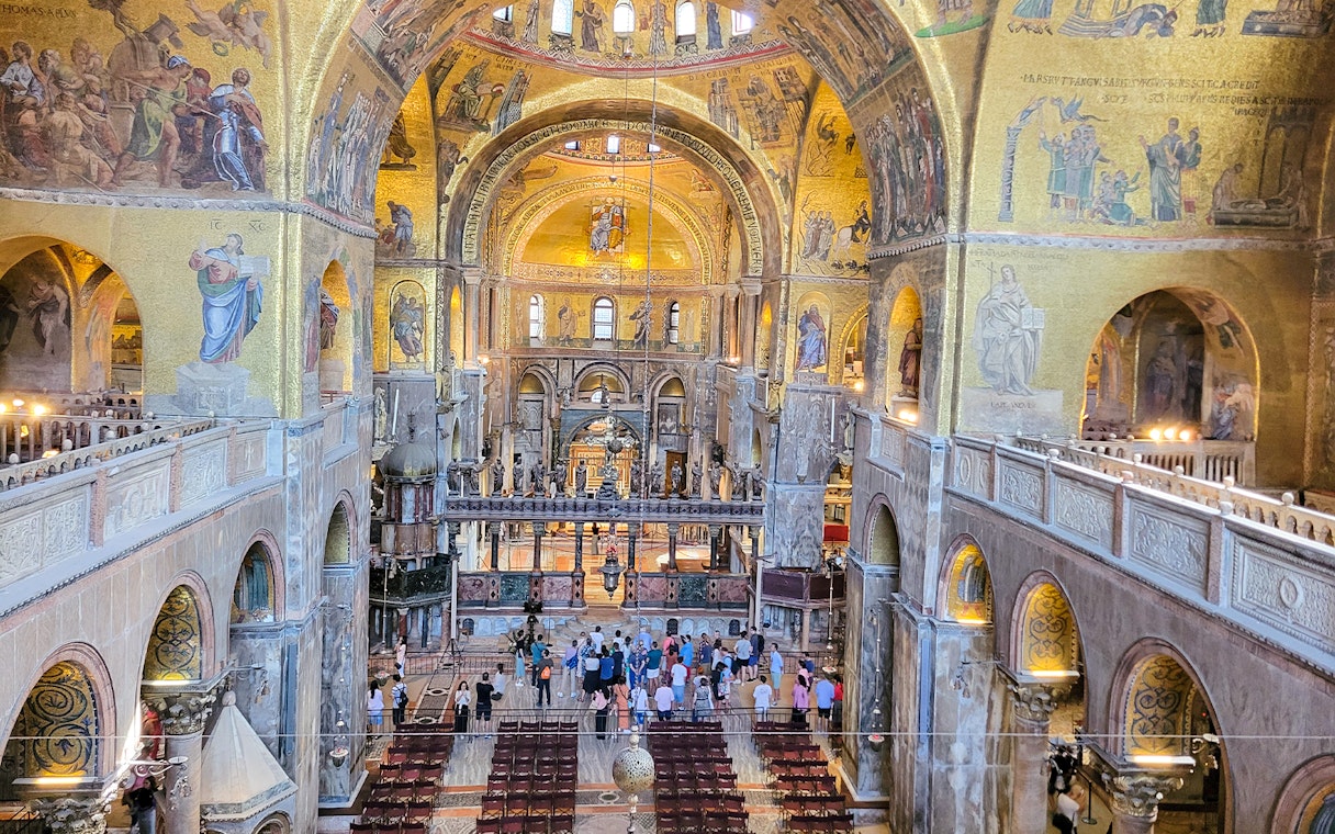 Interior view of St. Mark's Basilica with visitors and ornate mosaics, Venice, Italy.