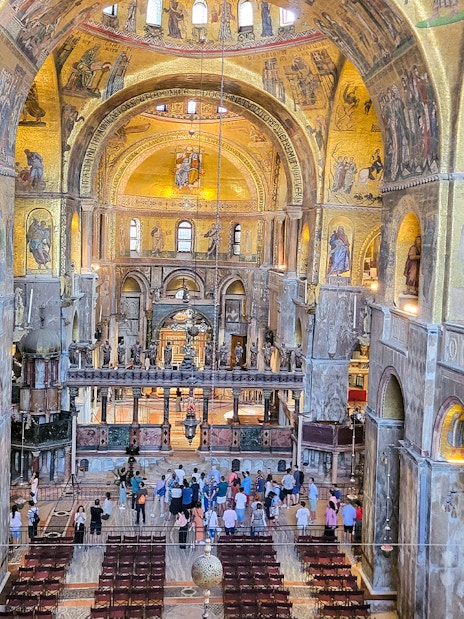 Interior view of St. Mark's Basilica with visitors and ornate mosaics, Venice, Italy.