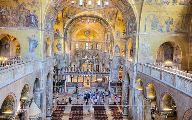 Interior view of St. Mark's Basilica with visitors and ornate mosaics, Venice, Italy.