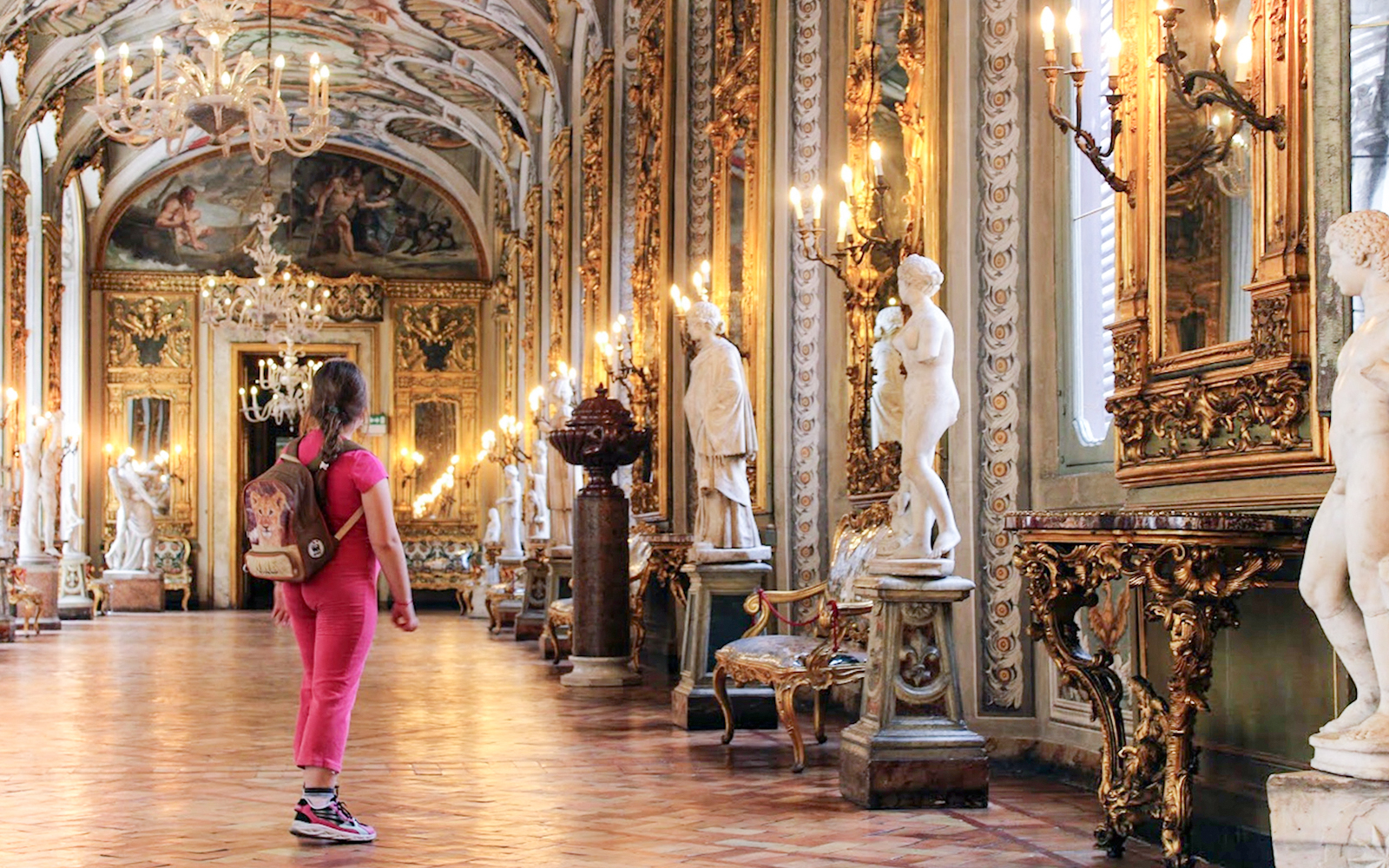 Girl exploring ornate hall with statues at Doria Pamphilj Gallery, Rome.