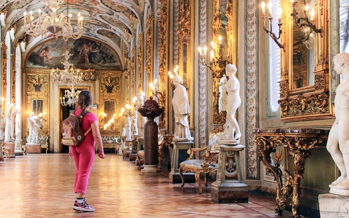 Girl exploring ornate hall with statues at Doria Pamphilj Gallery, Rome.