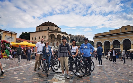 Group on electric bikes in Monastiraki Square, Athens, with Acropolis in background.