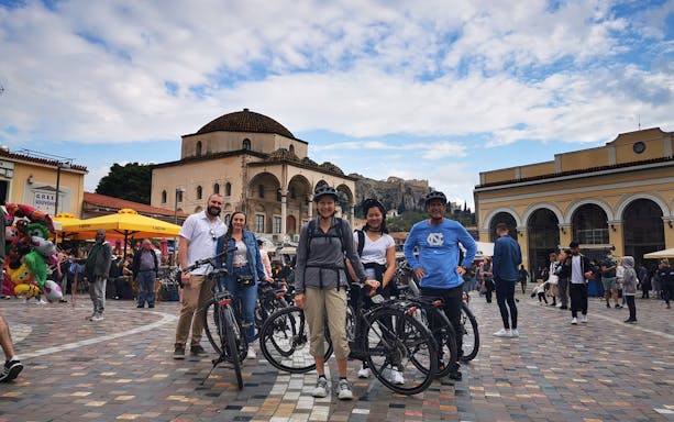 Group on electric bikes in Monastiraki Square, Athens, with Acropolis in background.