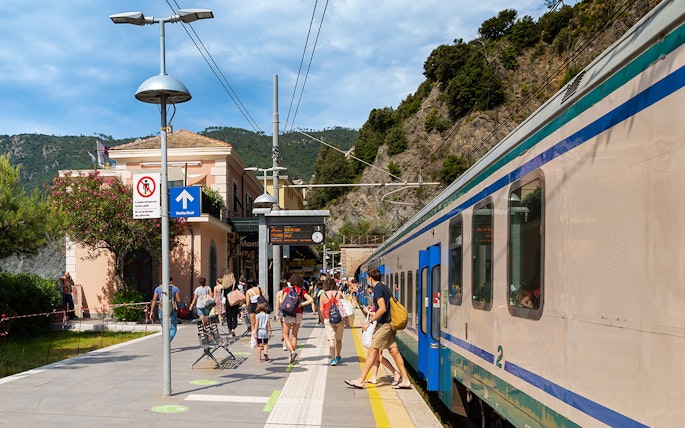 Travelers at a train station in Cinque Terre, Italy, boarding a train.
