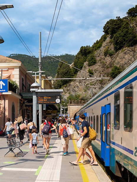Travelers at a train station in Cinque Terre, Italy, boarding a train.