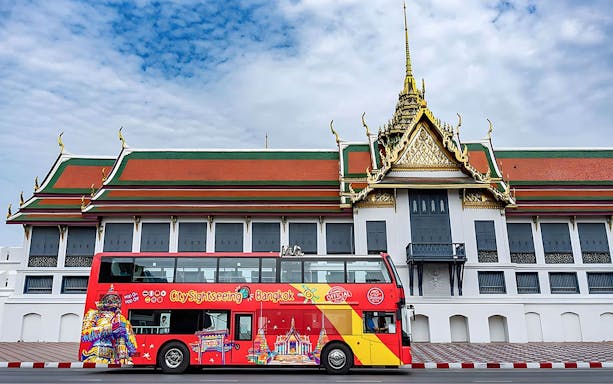 Red double-decker sightseeing bus in front of Bangkok's Grand Palace.