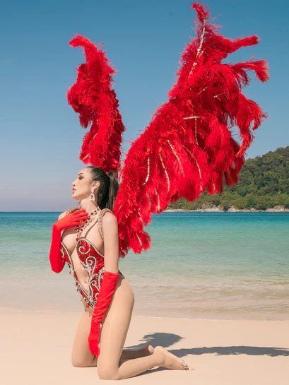Performer in red feathered costume on a beach, Simon Cabaret, Thailand.