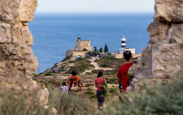 Hikers approaching lighthouse on Colle of Sant'Elia with sea view.