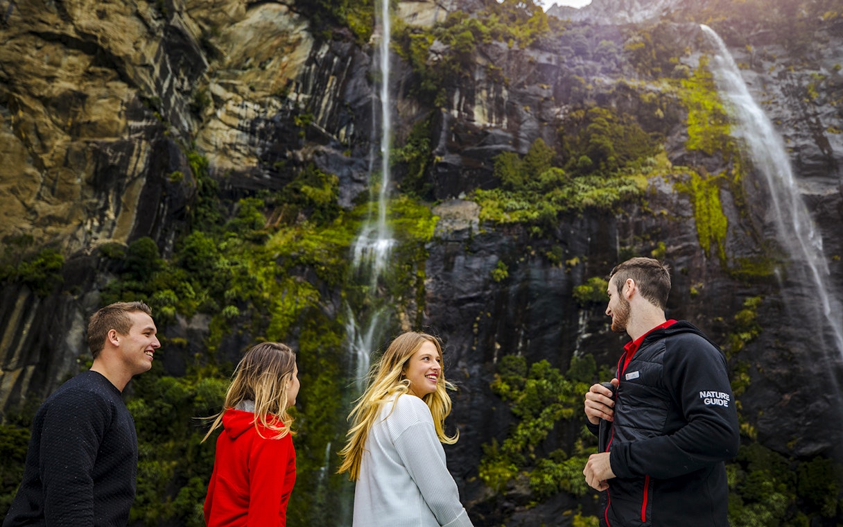 People enjoying a Milford Sound cruise with a nature guide, surrounded by waterfalls and lush cliffs.
