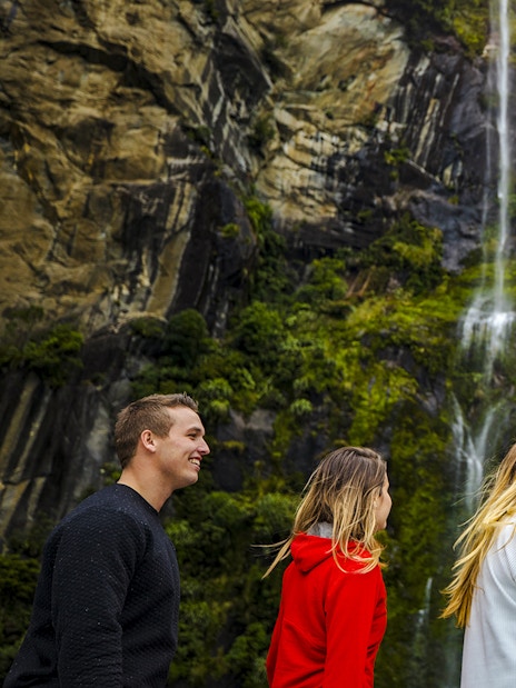 People enjoying a Milford Sound cruise with a nature guide, surrounded by waterfalls and lush cliffs.