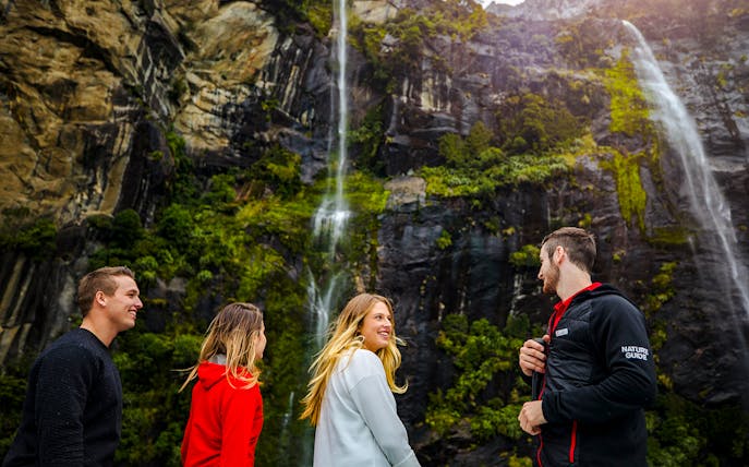 People enjoying a Milford Sound cruise with a nature guide, surrounded by waterfalls and lush cliffs.