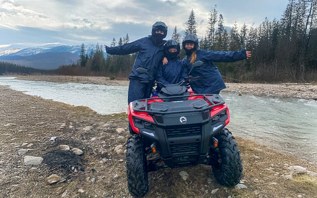 Visitors on a quad bike by a river in Zakopane, Poland, with mountains in the background.