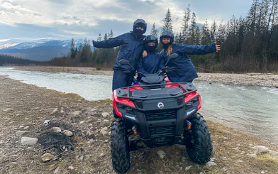 Visitors on a quad bike by a river in Zakopane, Poland, with mountains in the background.