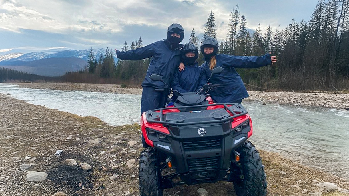 Visitors on a quad bike by a river in Zakopane, Poland, with mountains in the background.