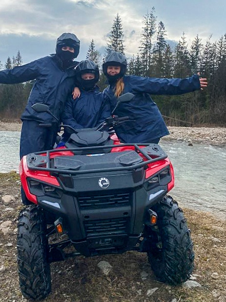 Visitors on a quad bike by a river in Zakopane, Poland, with mountains in the background.