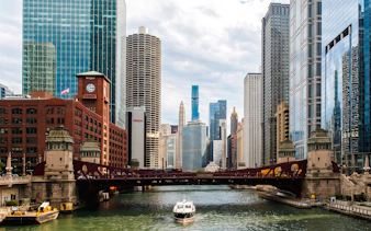 Chicago River cruise boat passing under LaSalle Street Bridge with city skyline.