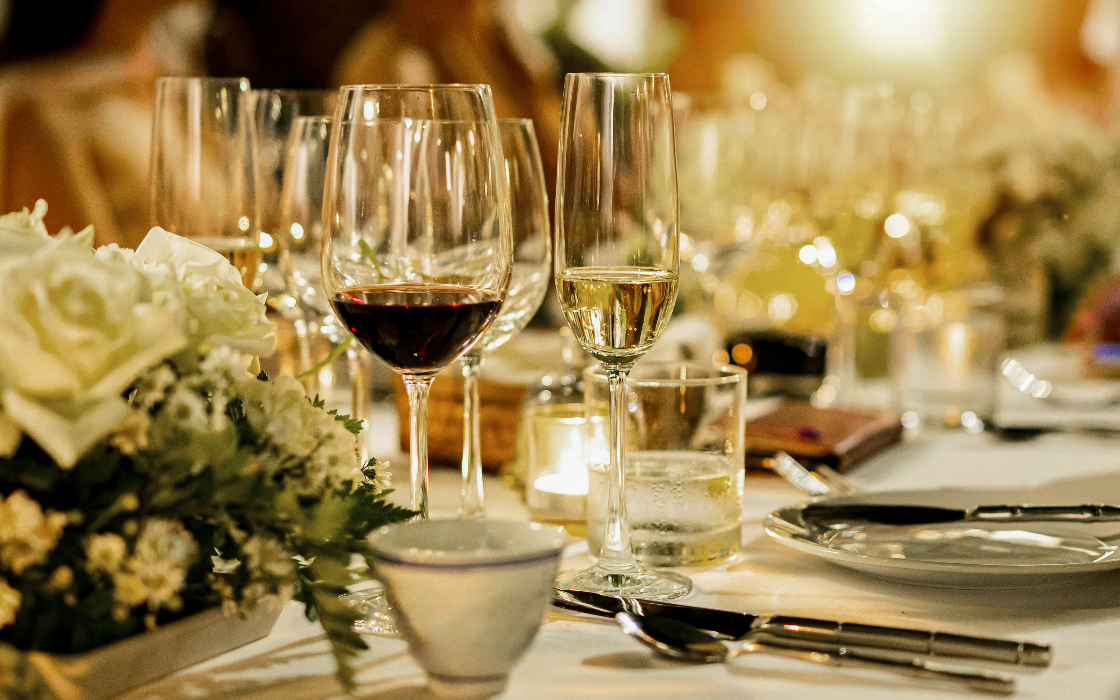 Red and white wine glasses on an elegant dining table with floral centerpiece.