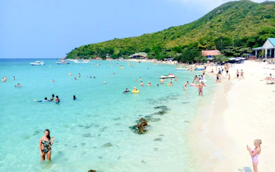 Tourists enjoying the beach and clear waters on Coral Island, Pattaya, with speedboats in the distance.