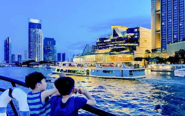 Yodsiam sightseeing boat with passengers on deck near Iconsiam, Bangkok skyline in background.