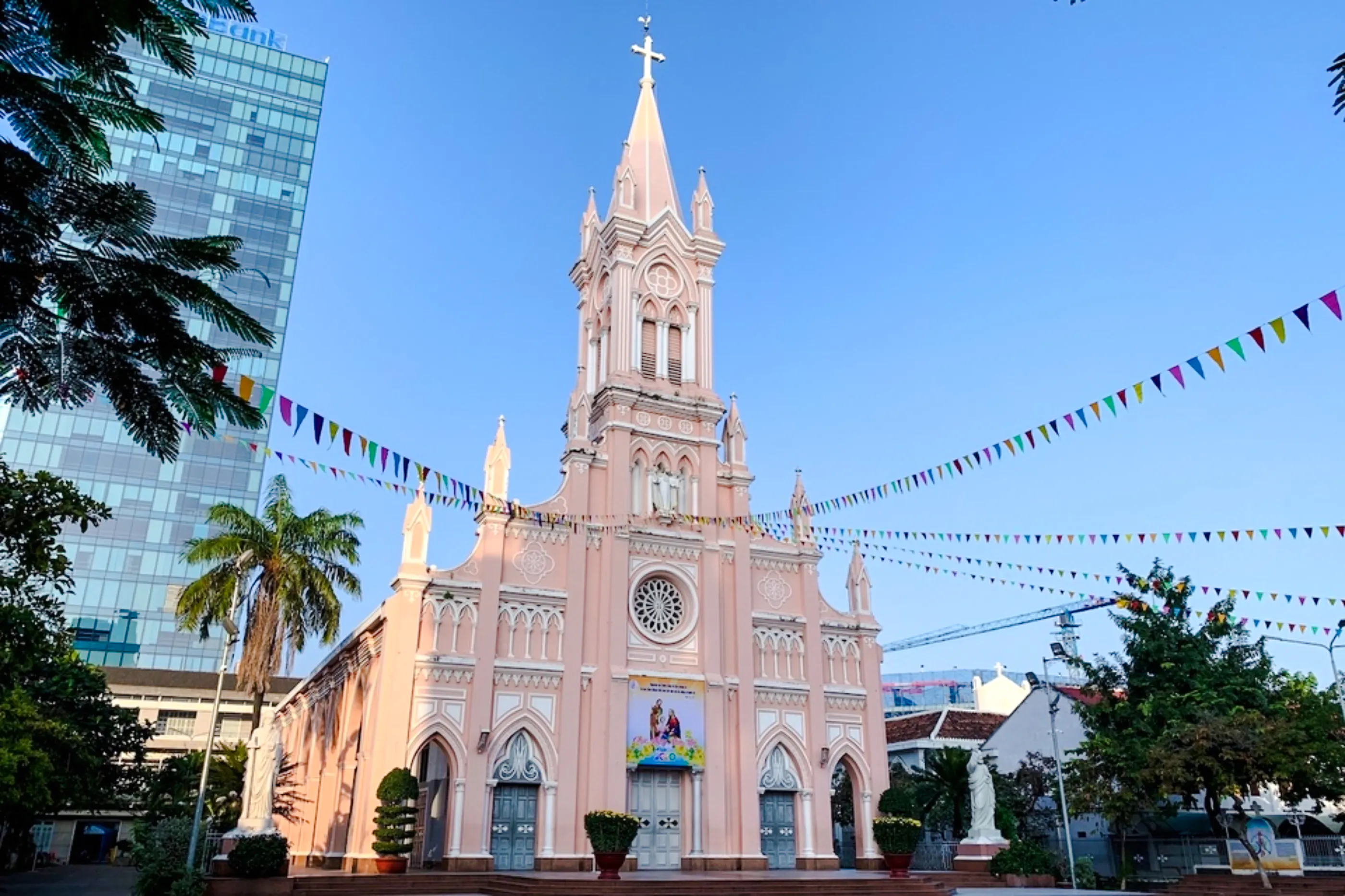 Pink Gothic-style cathedral in Da Nang with colorful flags and palm trees.
